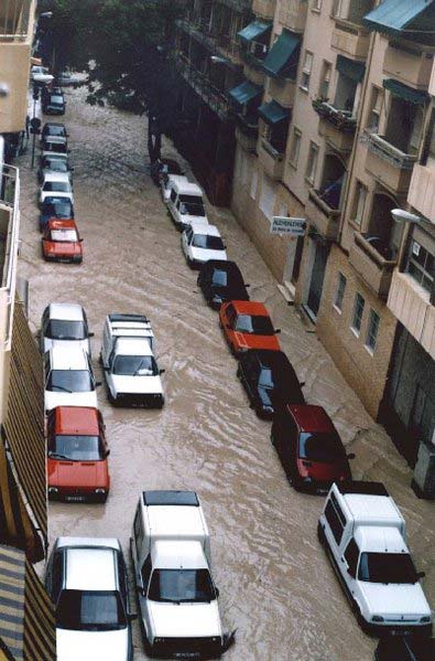 Looking down a flooded street from the view of an apartment window, this photo shows a large number of flooded cars that have been drenched in the heavy rainfall.