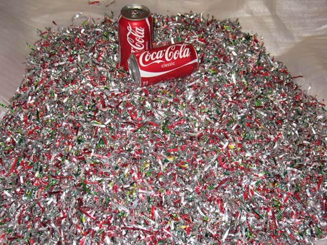 Two empty cans lie on a large pile of shredded aluminium cans which are being used for recycling purposes.