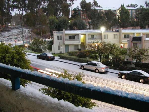 This photo shows a build up of snow after a night of heavy snowfall. The roads are covered in a layer of snow as well as the cars parked on the side of the street.