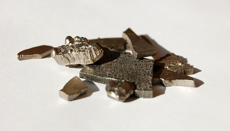 Chunks of solid cobalt can be seen in this photo. The different shaped pieces sit on a table which also serves as a white background.