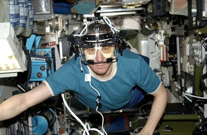 An astronaut experiments in gravity free space with an eye tracking device. The complicated equipment rests on the astronauts head as he floats around the shuttle.