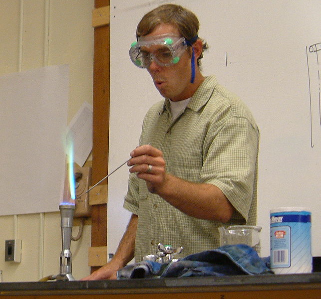 A scientist undertakes a flame test while wearing large protective goggles.