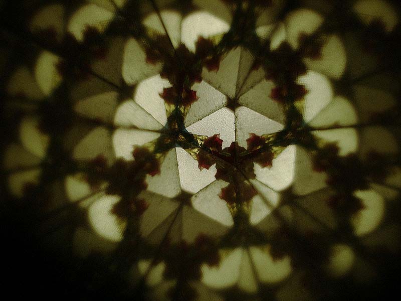 This photo shows the view from inside a kaleidoscope. The shapes and colors are reflected in a symmetrical pattern by the mirrors inside the kaleidoscope.