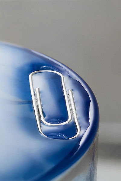 This excellent photo shows how the idea of surface tension works. A paper clip sits on top of the liquid in a glass, you can clearly see a skin which holds the paper clip above the surface.