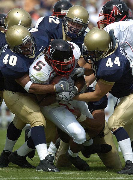 A team of defenders tackle an opposing player as he holds tightly to the ball during an American football game.