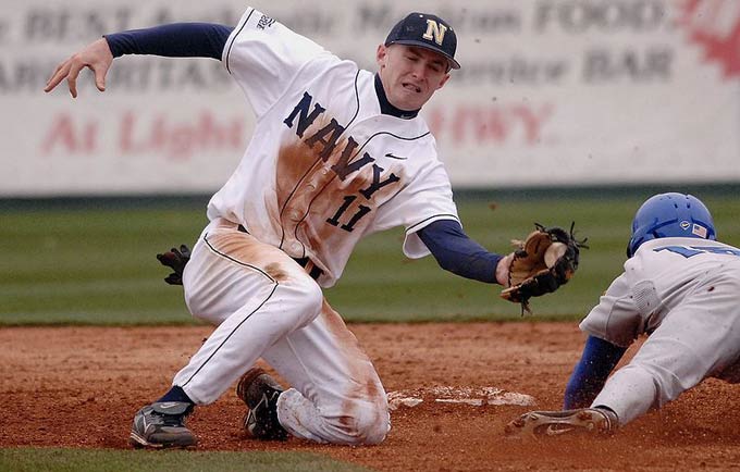A baseball player leans in to make a tag on an opposing player as he slides in to the base.