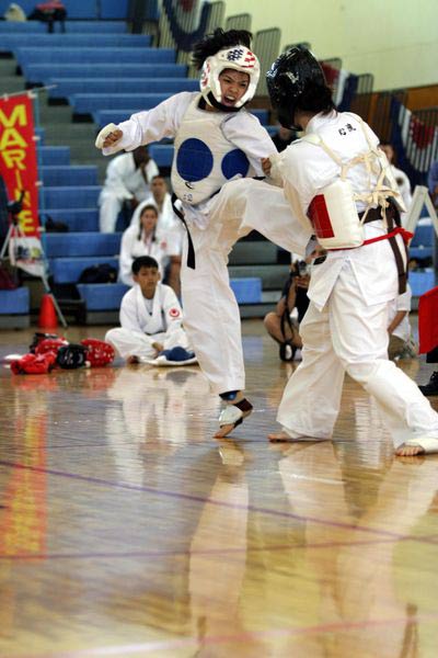 Two karate competitors battle it out in a competition, one defends herself as the other makes an attacking kick.