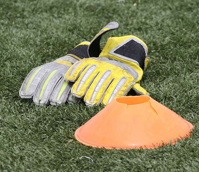 Two well worn football goalkeeper gloves sit on the grass behind a broken practice cone.