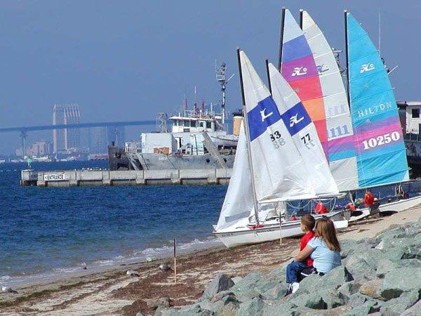 A group of small sailing boats sit on the sand on a beautiful sunny day.